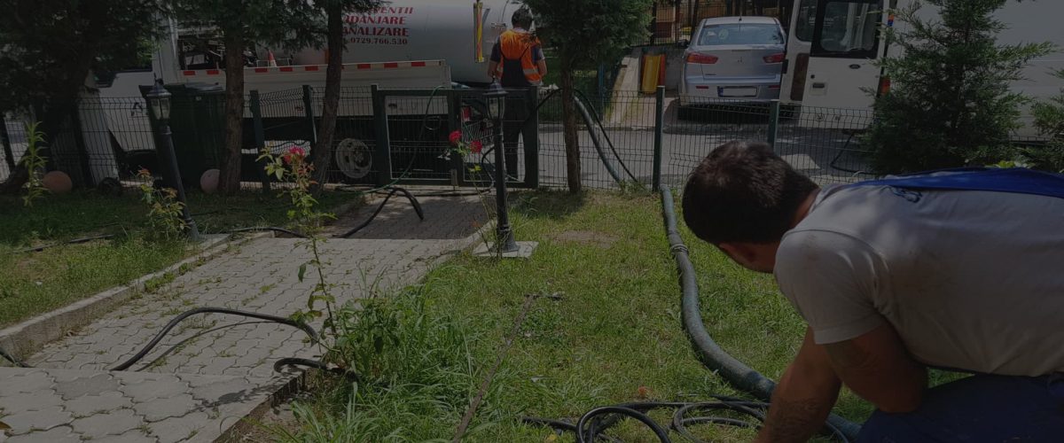 Operator care ține furtunul vidanjei în curtea unei case